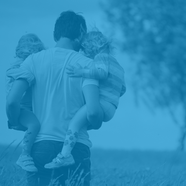 Dad carrying two little girls through a field